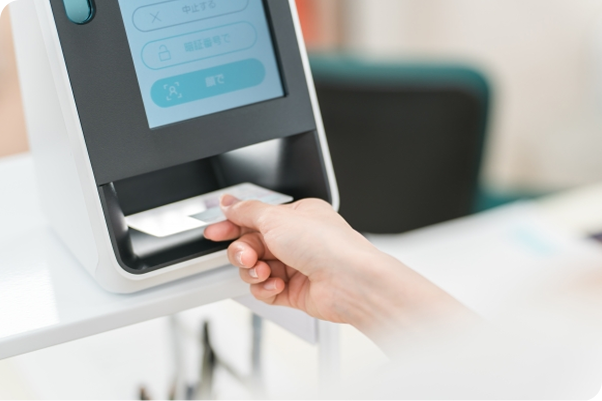 受付端末にカードを差し込む手元のクローズアップで、セルフサービス型の認証や支払い手続きを行う様子を表した場面