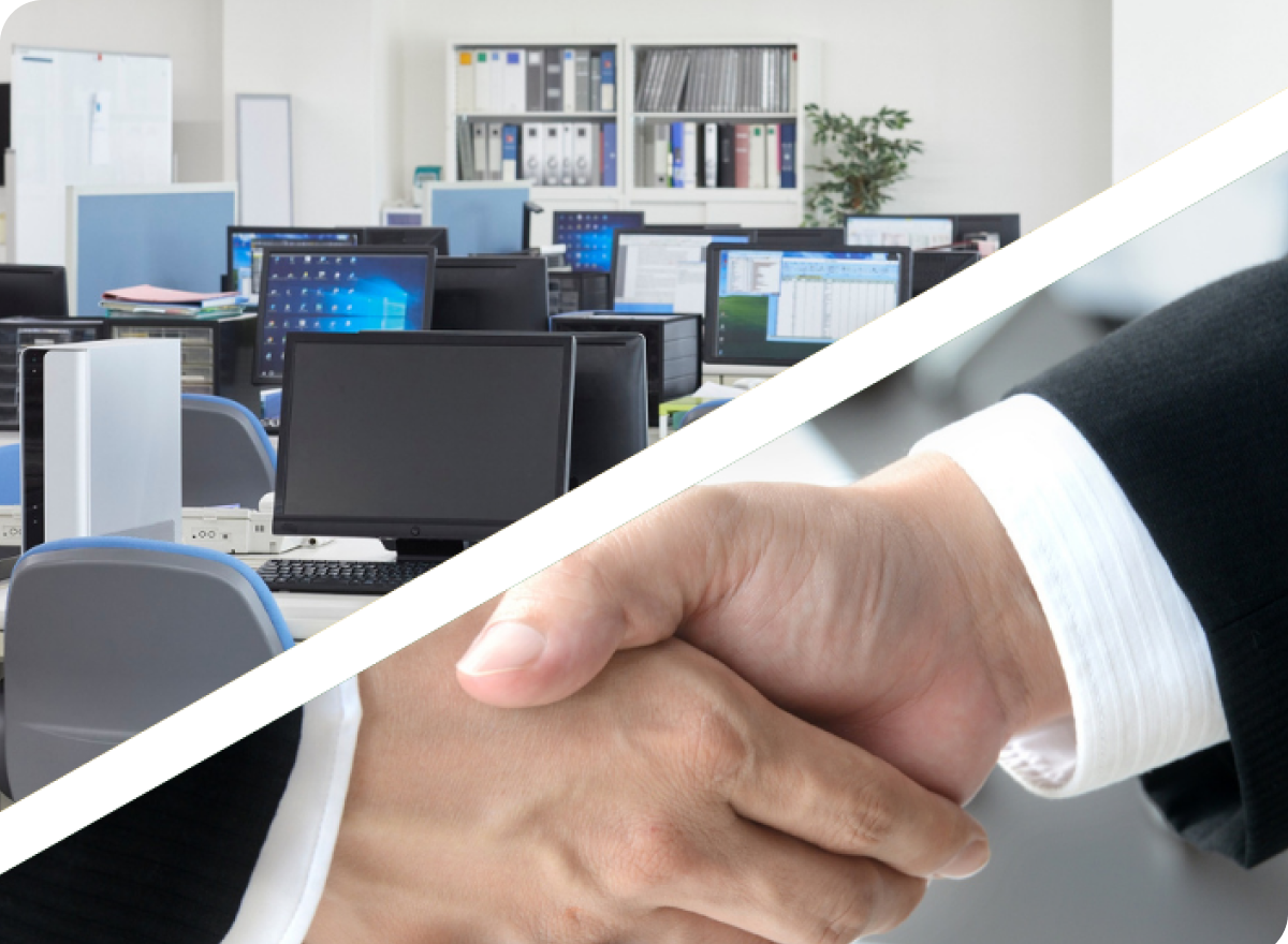 デスクトップPCが並ぶ職場環境と、スーツ姿の人物の握手を重ねた企業提携やビジネス協力を象徴する画像