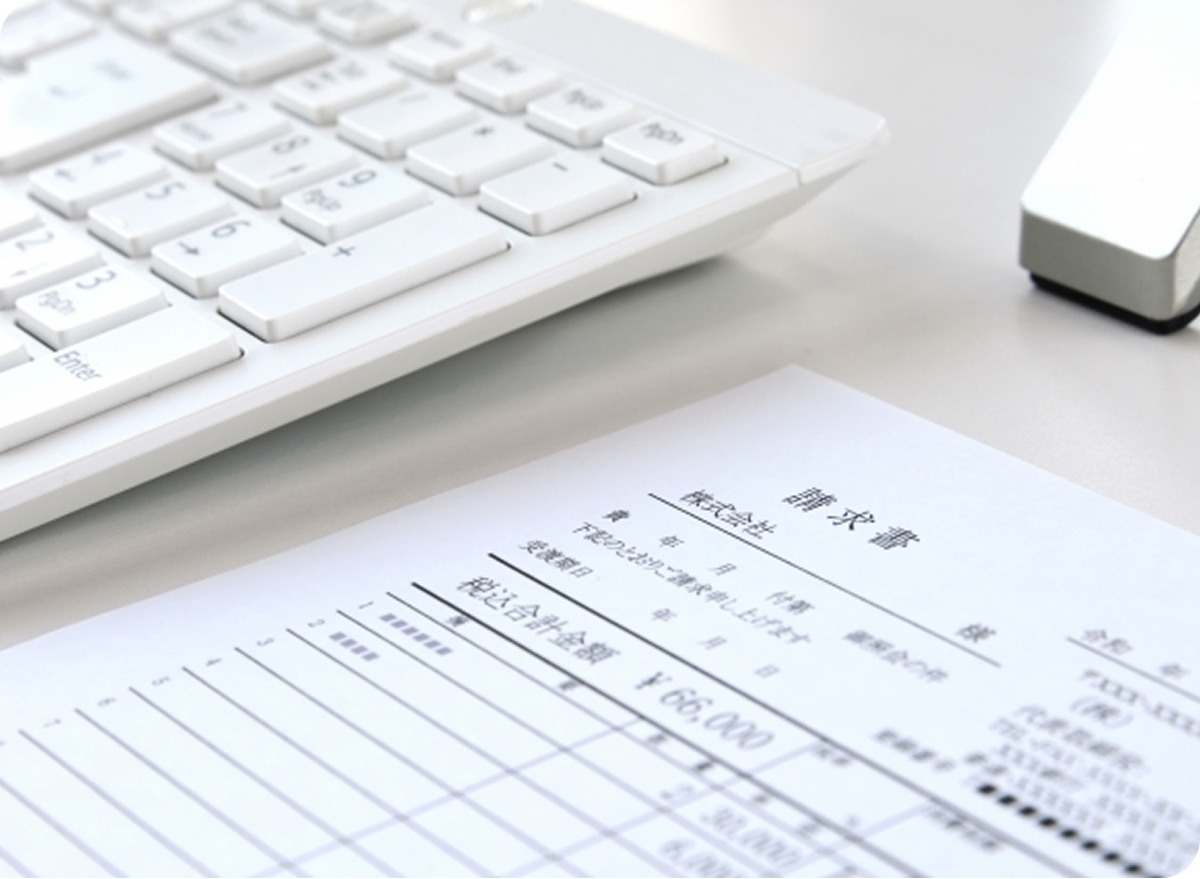 白いキーボードの横に請求書や明細書が置かれ、金額や項目が記載された書類を確認する事務作業の様子